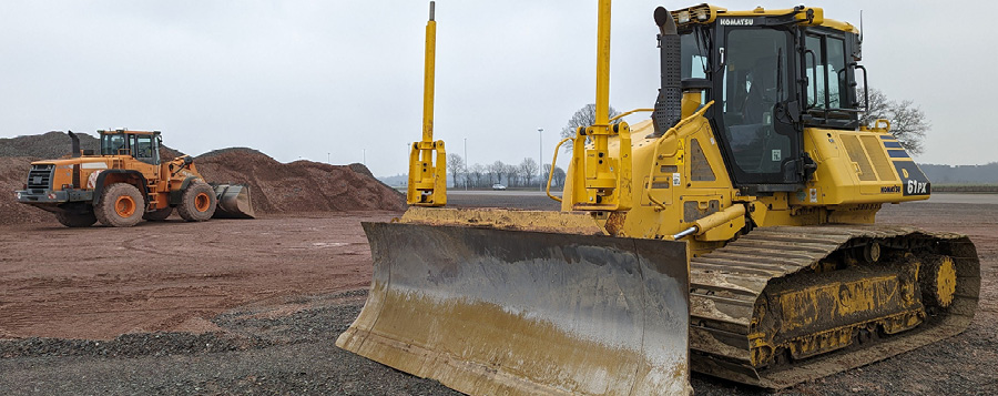 yellow dozer tractor on the right front-hand side of image with an orange dozer tractor in the back left of an image in a field of dirt with a dirt pile in the back left