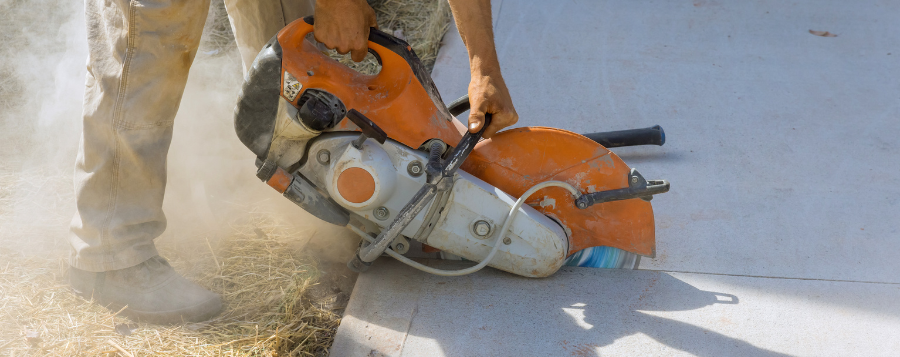 Man sawing concrete with concrete dust at his feet.